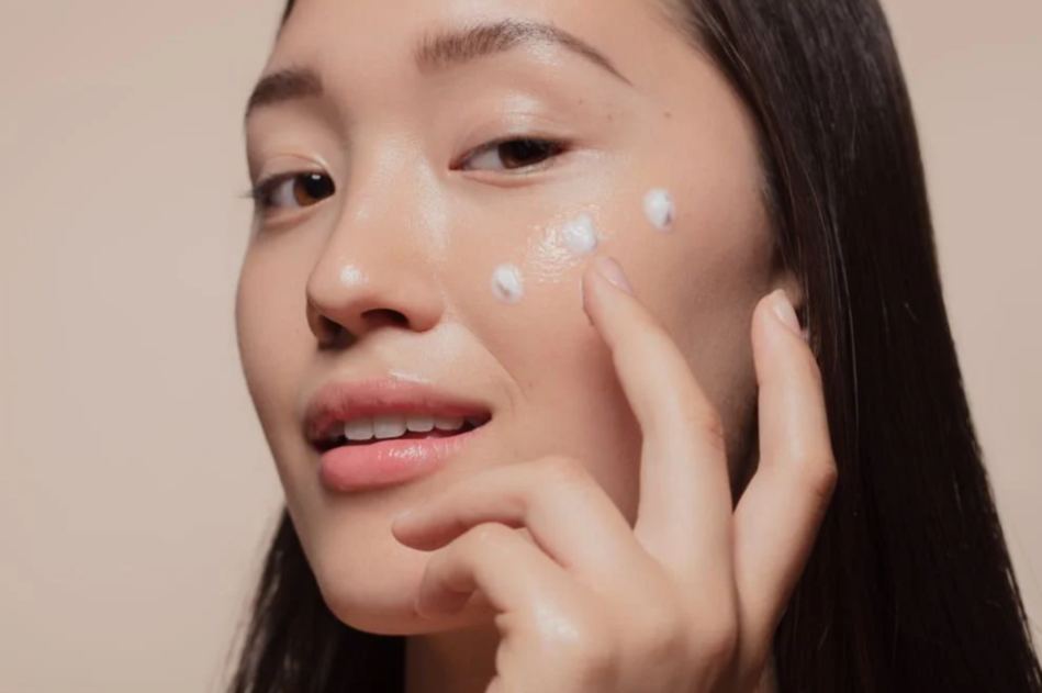 Woman applying cream to her cheek, healthy glowing skin