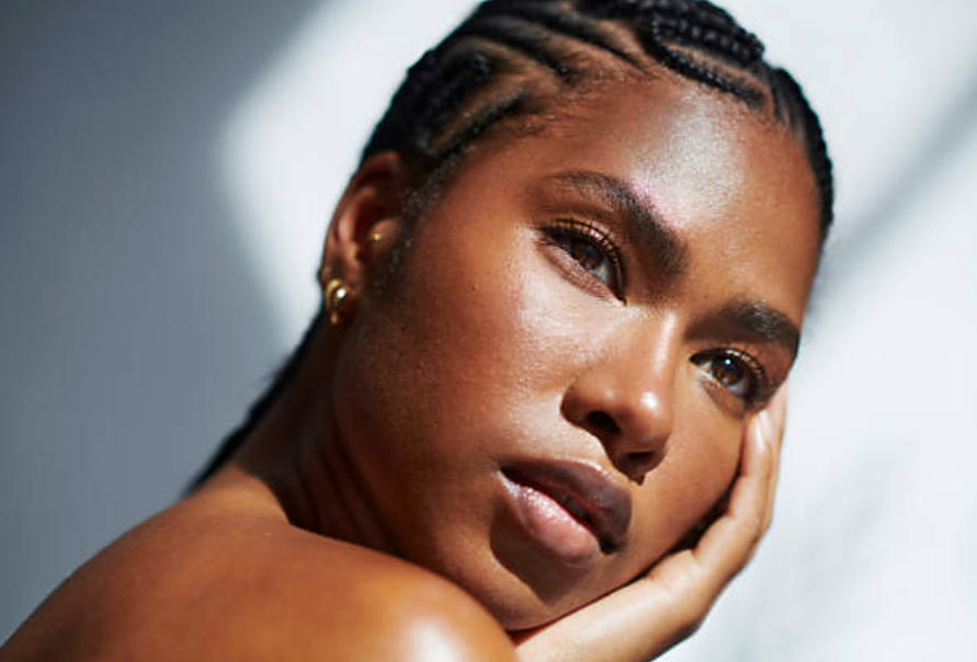 Woman with braided hair resting her face on her hand, glowing skin
